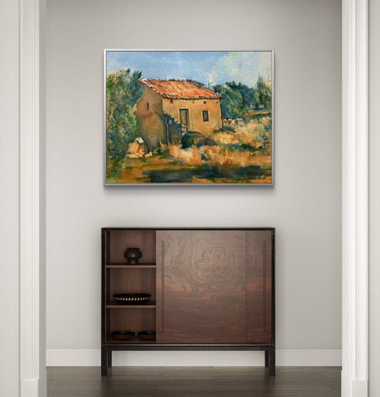 Framed painting of a rustic landscape above a wooden cabinet.