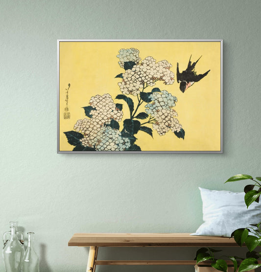 Framed artwork of flowers and a bird on a yellow background, displayed on a wall above a wooden bench.
