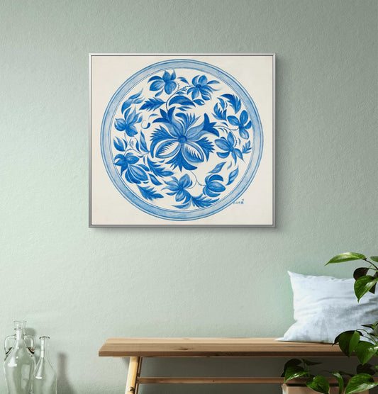 Framed blue floral artwork on a light green wall with a wooden bench and plant in the foreground.