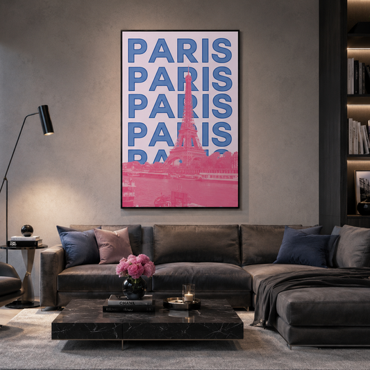 A framed vertical wall art print featuring the word 'PARIS' repeated in blue with a pink Eiffel Tower silhouette and pink lower section, displayed above a dark gray sectional sofa in a modern living room.