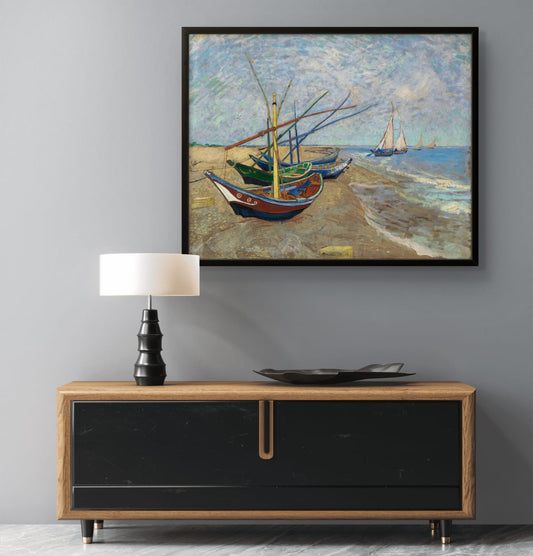 Framed painting of boats on a beach above a wooden console table with a lamp.