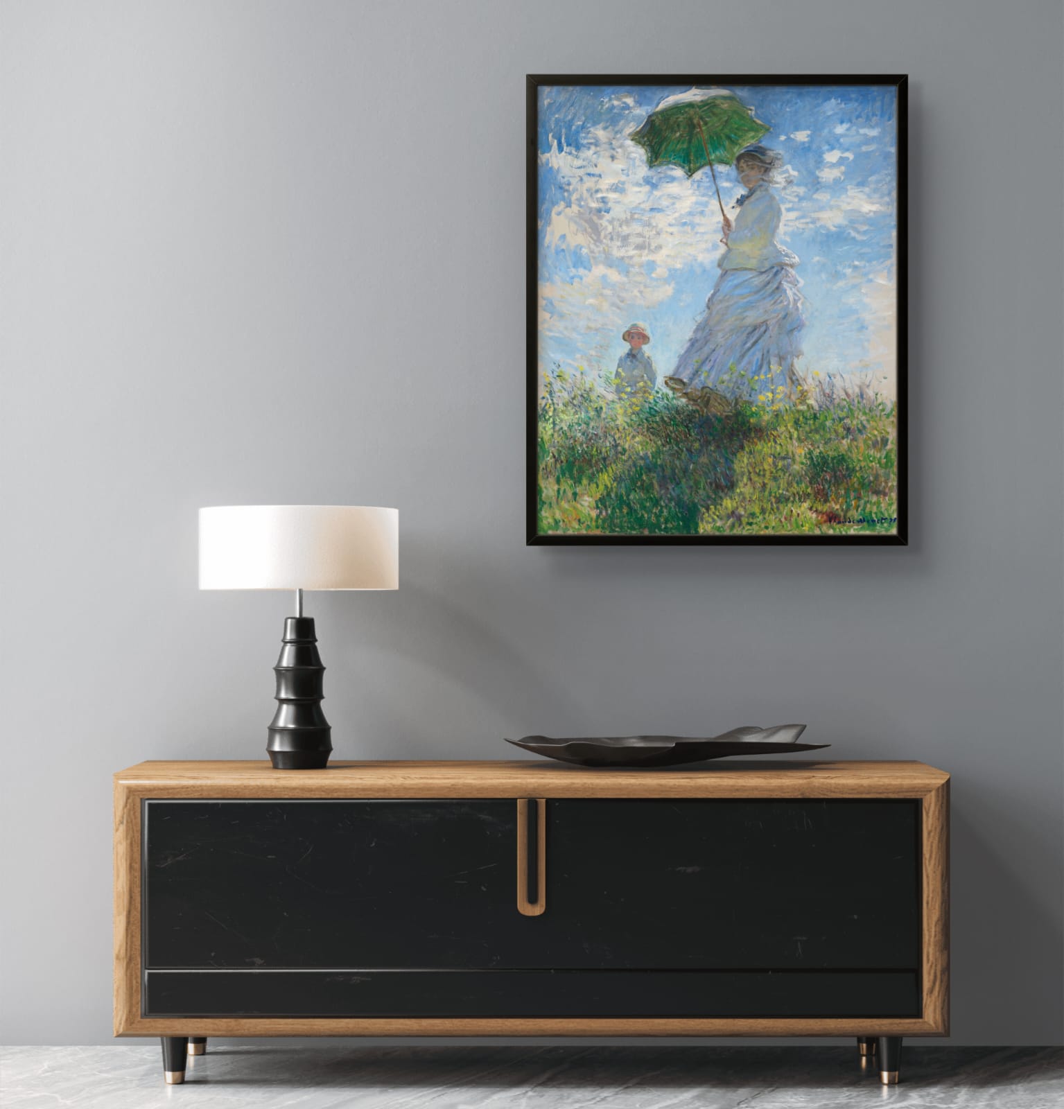 Framed painting of a woman with an umbrella above a wooden console table with a lamp and decorative plate.