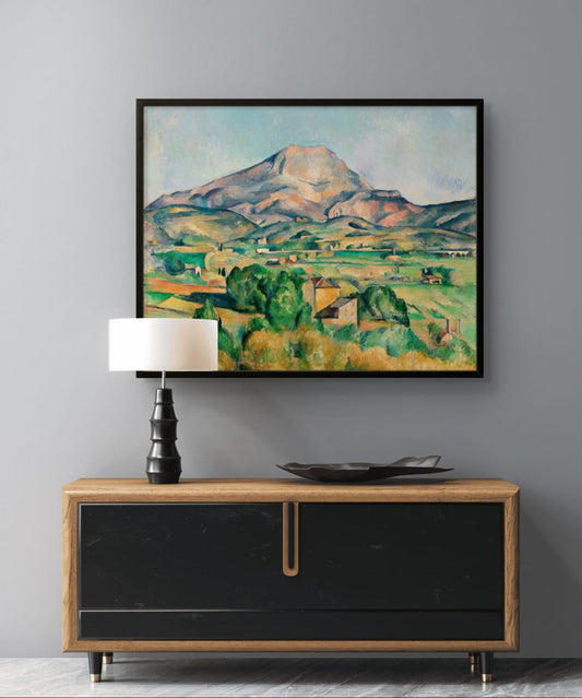 Framed painting of a mountain landscape above a wooden sideboard with a lamp.