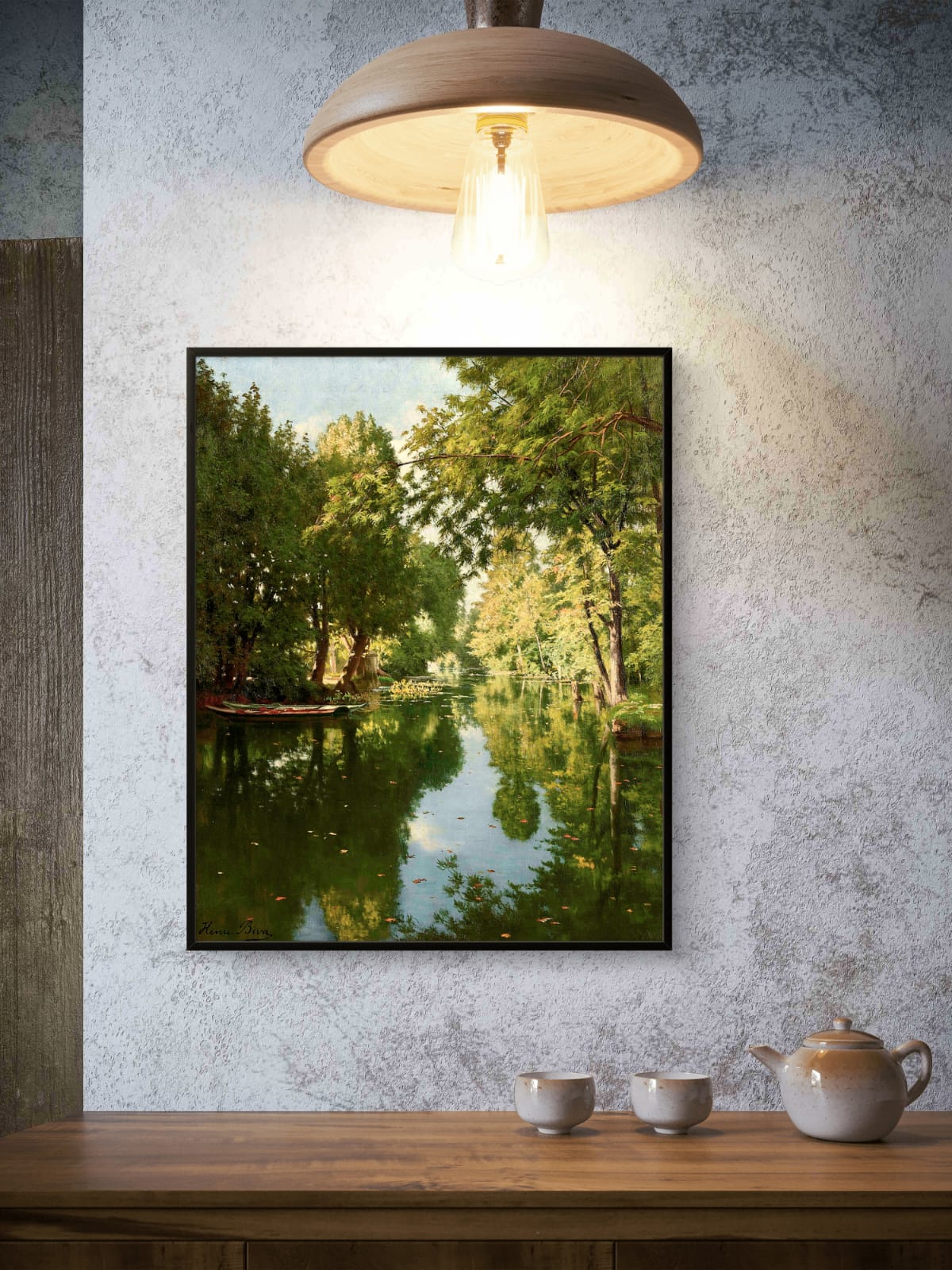 Framed nature print of a lake surrounded by trees on a textured wall above a wooden table with teacups and a teapot.