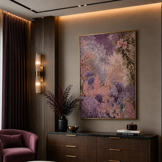A large framed abstract floral painting in shades of purple, pink, and lavender hangs on a warm taupe wall in a luxury bedroom. The room features a dark wood dresser with gold handles, a plush mauve armchair, and a bed with matching purple bedding in the foreground.